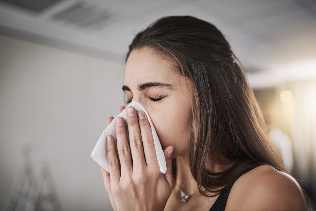 Flu seasons coming knocking. Shot of a young woman blowing her nose.