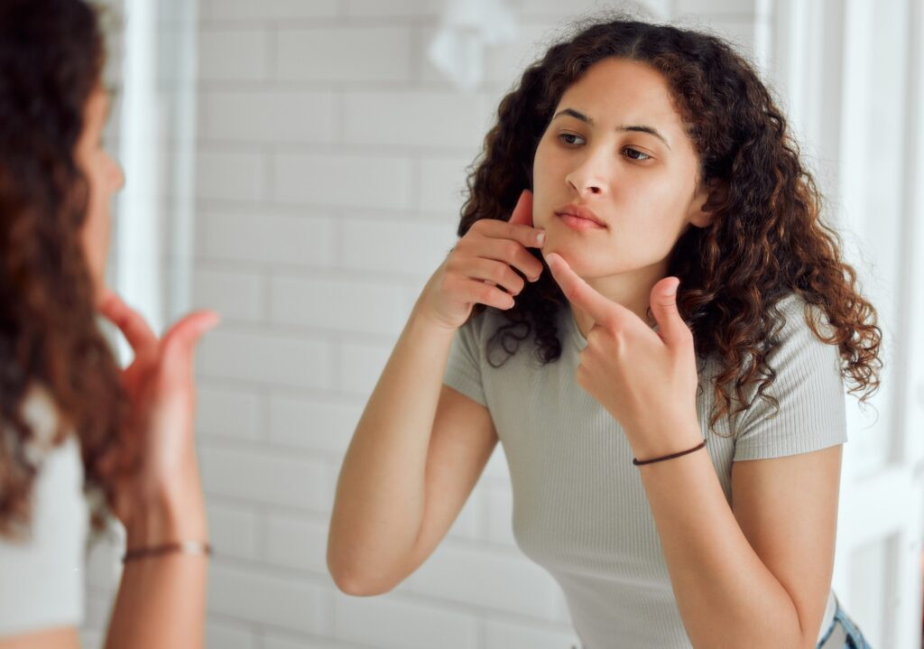 Unhappy, upset or annoyed woman popping a zit during a skincare routine while in front of a mirror